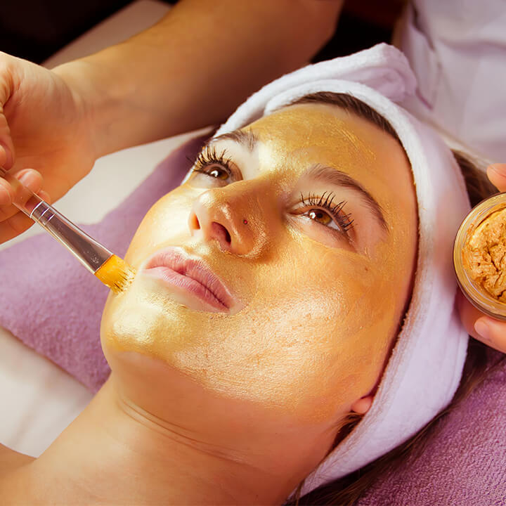 Client relaxing during a luxurious golden facial mask treatment applied with a brush, pampering at a serene beauty clinic.