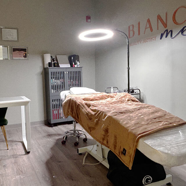 A cozy and well-equipped treatment room at Bonita Hub, with a plush-covered beauty bed under a bright circular light.