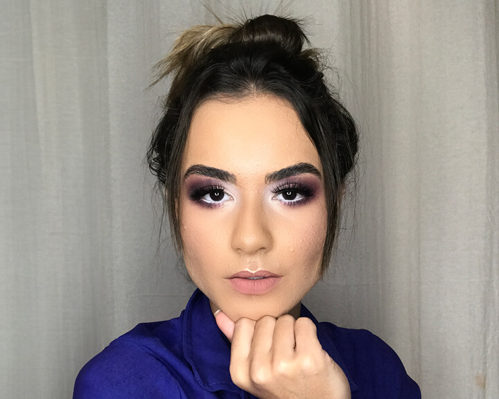 Makeup Artist Myllena showcasing her craft with a striking purple eyeshadow look and a poised expression.