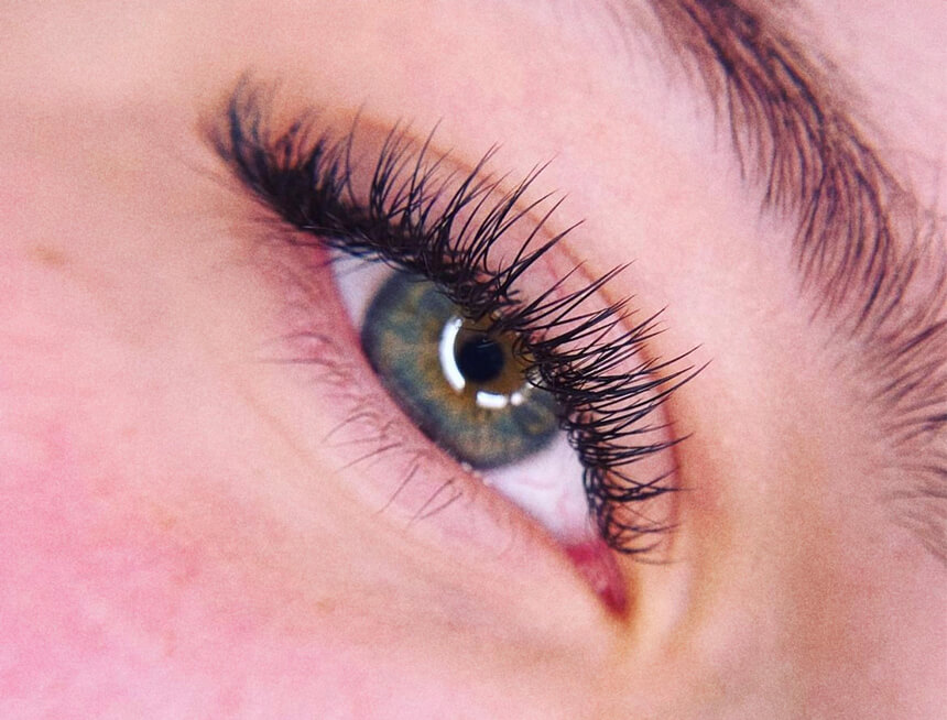 Close-up of a detailed view showcasing a green eye with extended, voluminous eyelashes, emphasizing precise lash work.