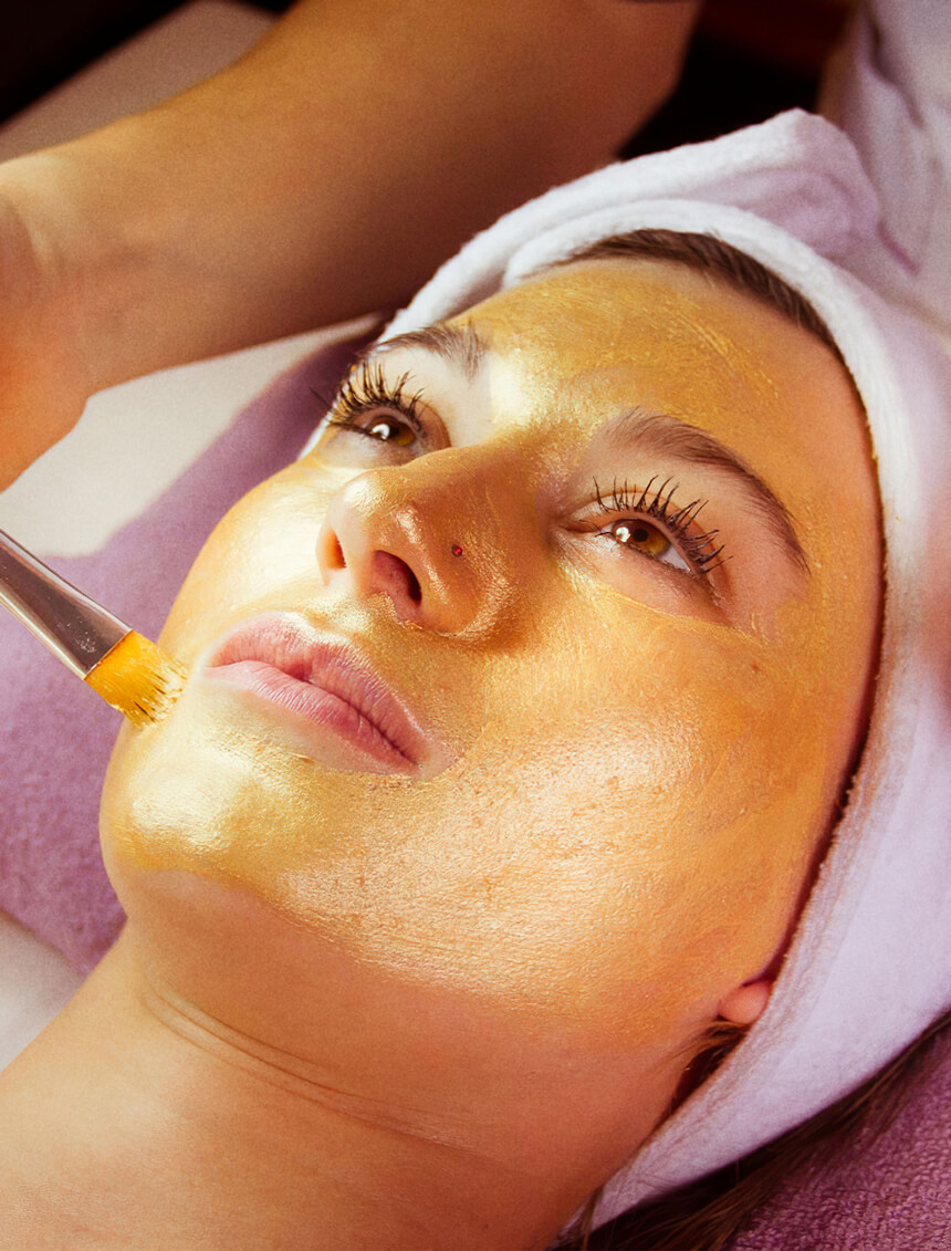 Client relaxing during a luxurious golden facial mask treatment applied with a brush, pampering at a serene beauty clinic.