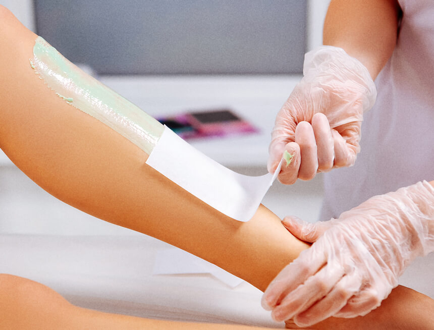 Professional aesthetician carefully peels off a waxing strip from a client's leg, demonstrating a hair removal procedure in a clinical setting.