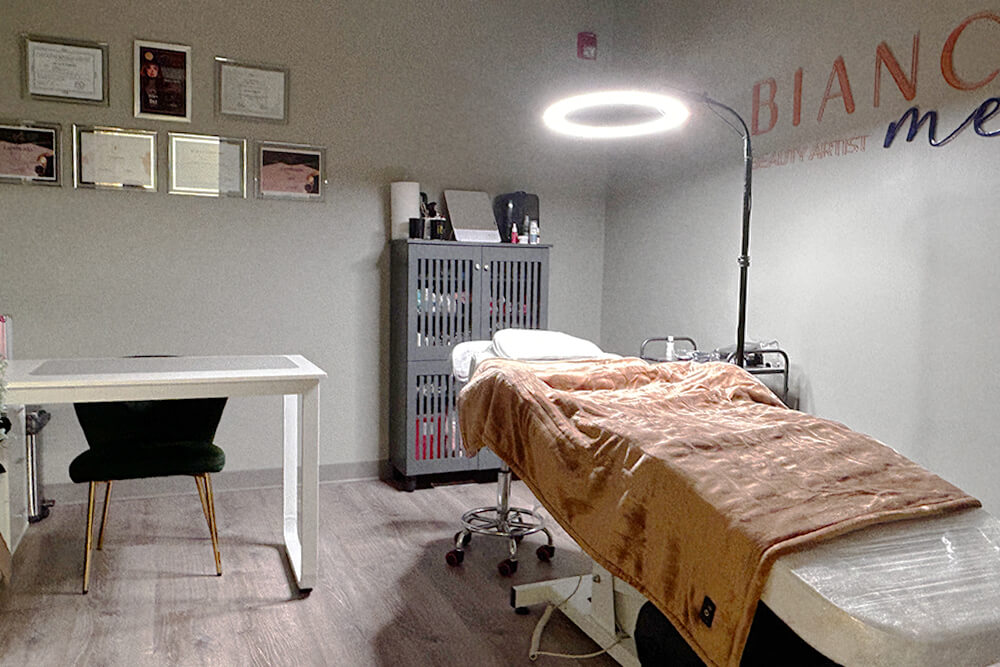 A cozy and well-equipped treatment room at Bonita Hub, with a plush-covered beauty bed under a bright circular light.